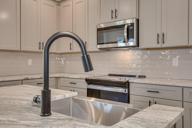 kitchen with gray cabinetry, appliances with stainless steel finishes, decorative backsplash, and light stone counters