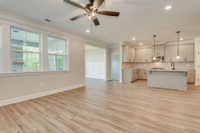 kitchen featuring ornamental molding, open floor plan, light countertops, stainless steel microwave, and tasteful backsplash