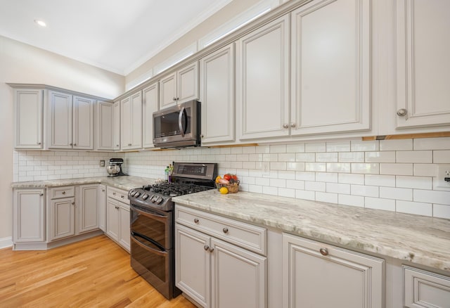 kitchen with crown molding, light stone counters, decorative backsplash, light wood-style flooring, and appliances with stainless steel finishes