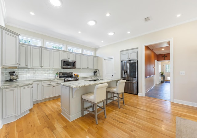 kitchen featuring visible vents, a breakfast bar, a sink, decorative backsplash, and appliances with stainless steel finishes