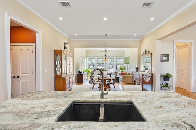 kitchen with crown molding, light stone countertops, visible vents, and a sink