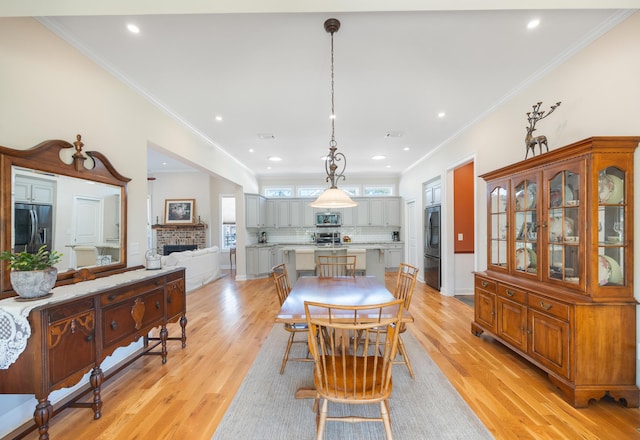 dining space featuring crown molding, a brick fireplace, and light wood-style floors