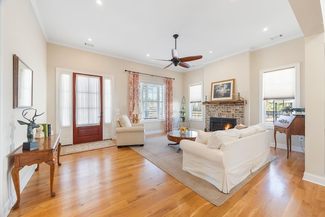 living room featuring baseboards, visible vents, crown molding, a brick fireplace, and light wood-type flooring