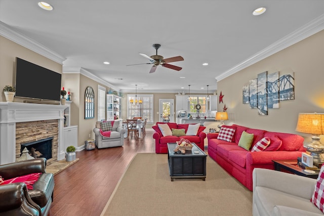 living room with crown molding, a stone fireplace, ceiling fan, and hardwood / wood-style flooring