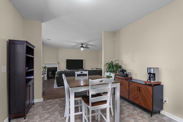 dining space with a ceiling fan, baseboards, light floors, and a fireplace