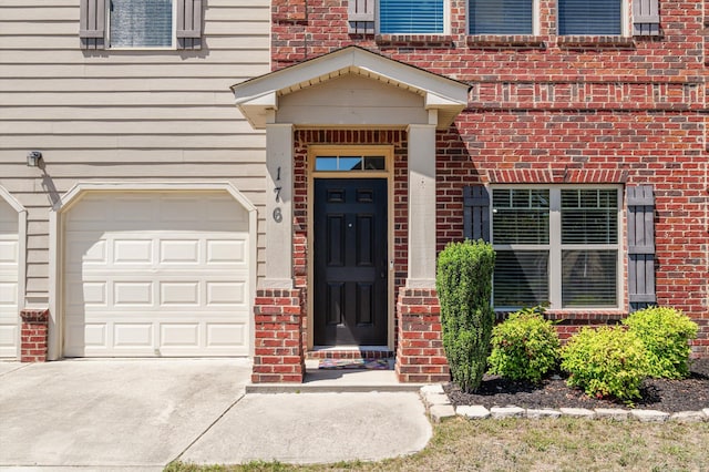 doorway to property with brick siding, a garage, and concrete driveway