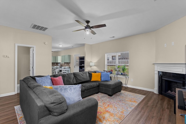 living room featuring visible vents, dark wood-style flooring, a fireplace, baseboards, and a ceiling fan