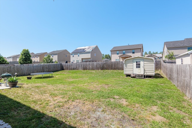 view of yard featuring a trampoline, an outbuilding, a residential view, a fenced backyard, and a storage unit
