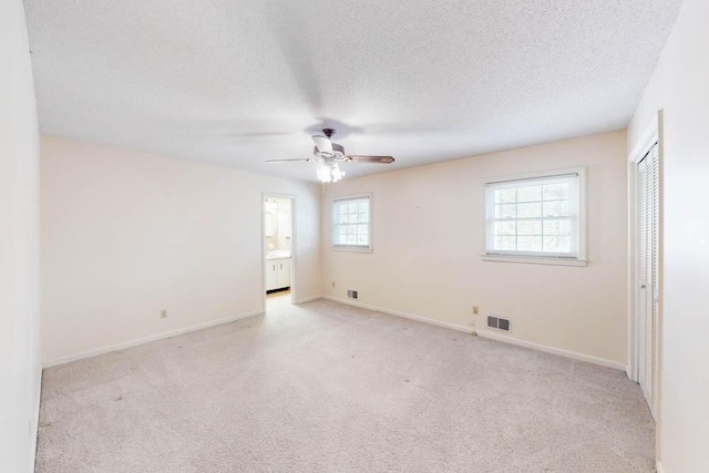 empty room with a textured ceiling, light colored carpet, and ceiling fan