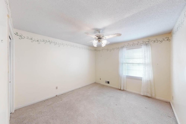 empty room with a textured ceiling, light colored carpet, and ceiling fan