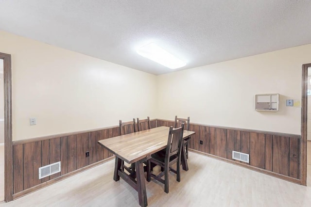 dining area featuring wood walls, light wood-type flooring, and a textured ceiling