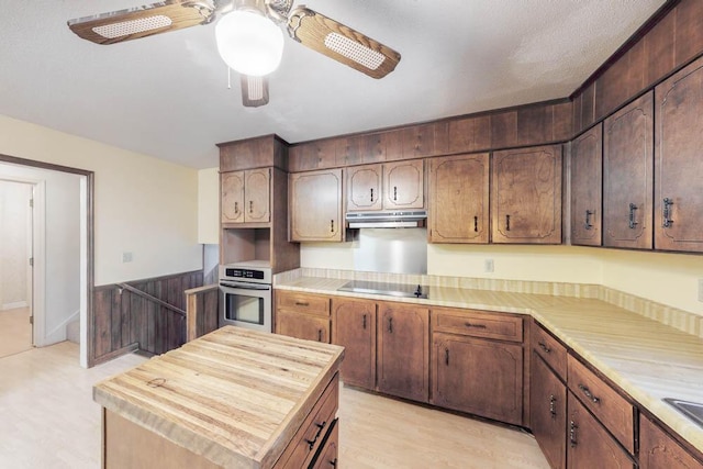 kitchen featuring black electric cooktop, ceiling fan, wooden walls, light hardwood / wood-style floors, and oven