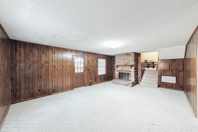 unfurnished living room with a fireplace, a textured ceiling, light colored carpet, and wooden walls