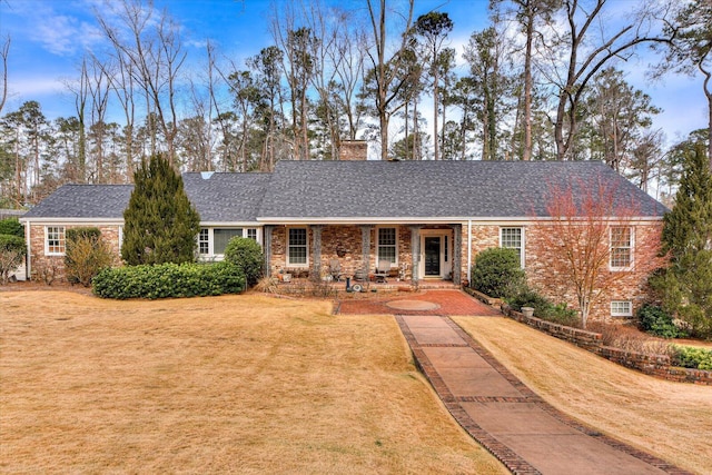 ranch-style house with brick siding, a shingled roof, a chimney, and a front yard