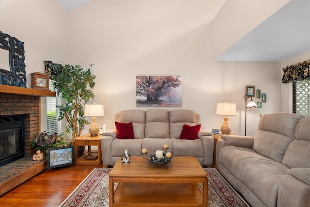 living area featuring a brick fireplace, wood finished floors, and a healthy amount of sunlight