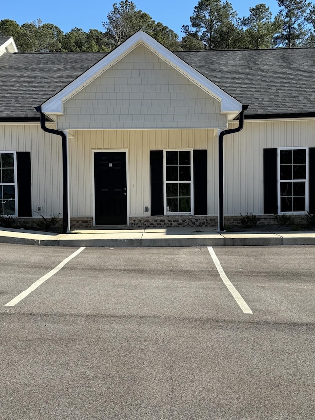 view of exterior entry with uncovered parking, board and batten siding, and roof with shingles