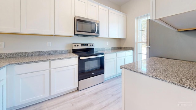 kitchen with light wood finished floors, appliances with stainless steel finishes, white cabinets, and a sink