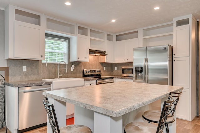 1711 Carolyn Lake Cir, Thomson, GA 30824 - kitchen with stainless steel appliances, open shelves, under cabinet range hood, a breakfast bar area, and white cabinets
