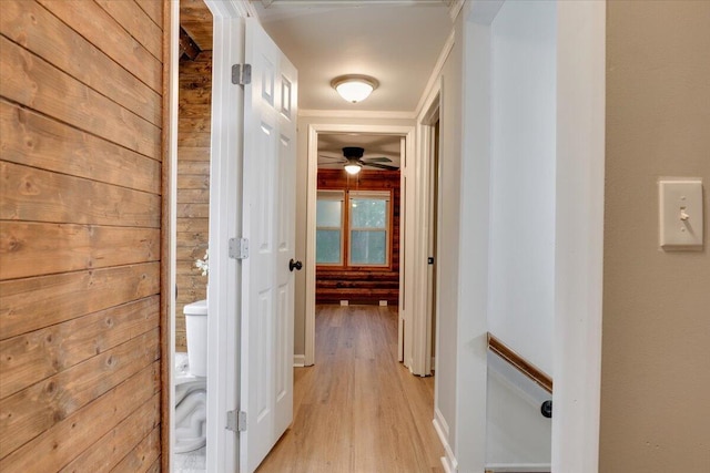 corridor featuring light wood-type flooring, crown molding, and wooden walls