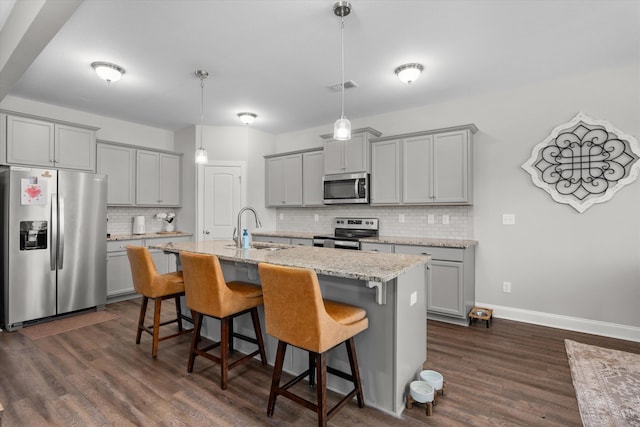 kitchen with an island with sink, appliances with stainless steel finishes, pendant lighting, light stone counters, and sink