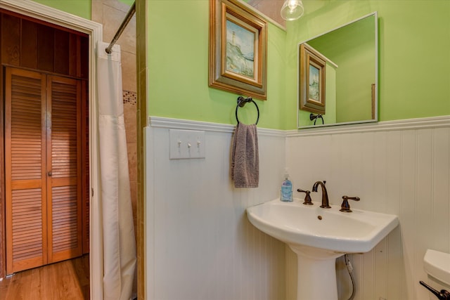 bathroom with a wainscoted wall, toilet, a shower with shower curtain, and wood finished floors