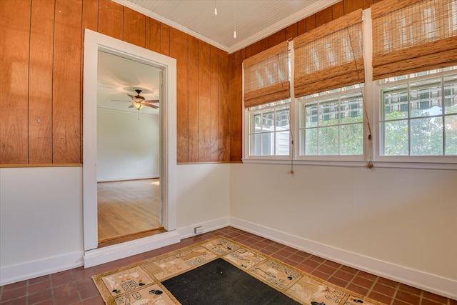 tiled empty room with ceiling fan, baseboards, wooden walls, and crown molding