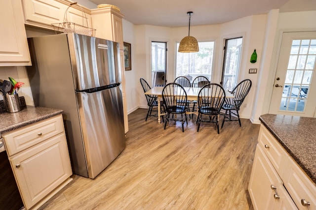 kitchen with tasteful backsplash, cream cabinets, light hardwood / wood-style flooring, stainless steel refrigerator, and hanging light fixtures