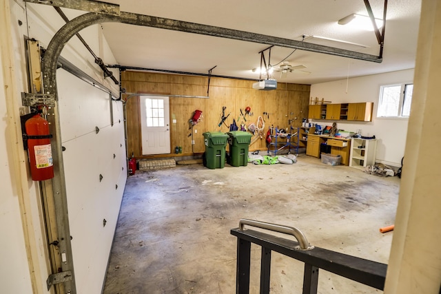 garage with a garage door opener, ceiling fan, and wood walls