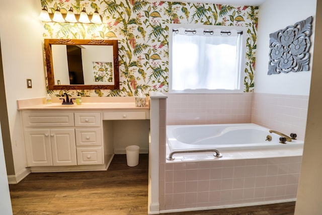 bathroom with wood-type flooring, vanity, and a relaxing tiled tub