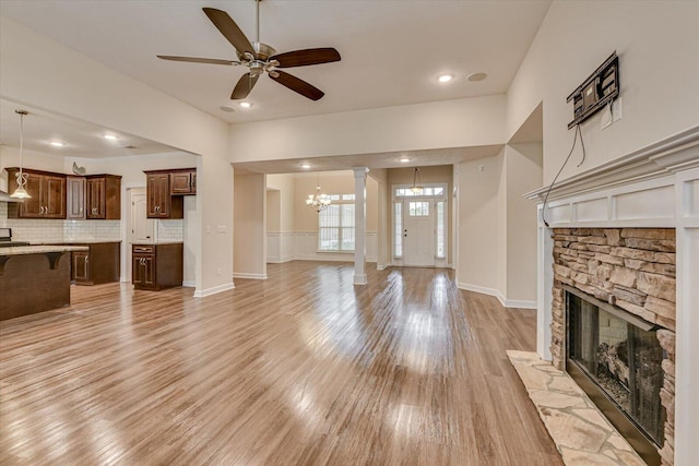 unfurnished living room featuring ornate columns, ceiling fan with notable chandelier, a fireplace, and light wood-type flooring