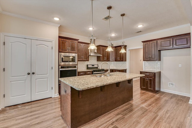 kitchen with sink, decorative light fixtures, stainless steel appliances, light stone countertops, and a kitchen island with sink