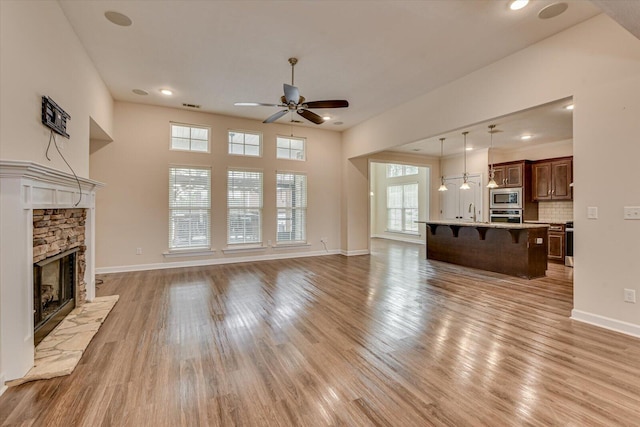 unfurnished living room with ceiling fan, a fireplace, and light hardwood / wood-style flooring