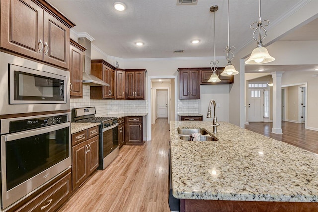 kitchen with appliances with stainless steel finishes, sink, hanging light fixtures, and a center island with sink