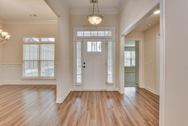 entrance foyer with a notable chandelier, ornamental molding, and light wood-type flooring