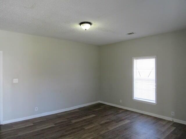 spare room featuring dark wood-style floors, a textured ceiling, visible vents, and baseboards