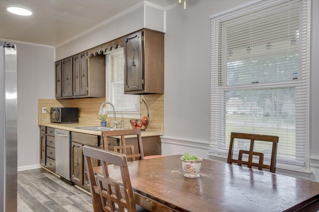 kitchen with sink, light hardwood / wood-style flooring, decorative backsplash, ornamental molding, and stainless steel appliances