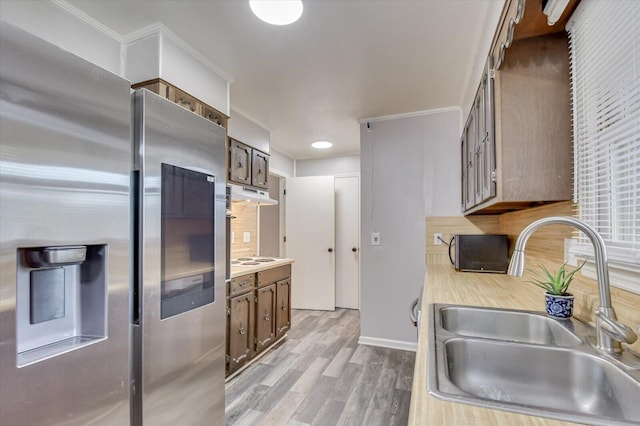 kitchen with stainless steel fridge, tasteful backsplash, ornamental molding, sink, and light hardwood / wood-style floors