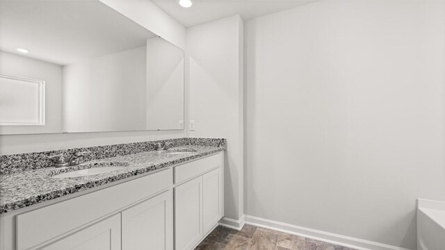 bathroom featuring double vanity, a washtub, baseboards, and a sink