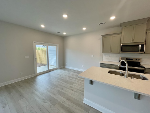 kitchen featuring a breakfast bar, sink, appliances with stainless steel finishes, tasteful backsplash, and light stone counters