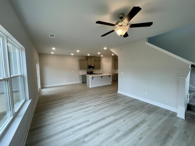 unfurnished living room with light wood-type flooring, ceiling fan, a healthy amount of sunlight, and sink