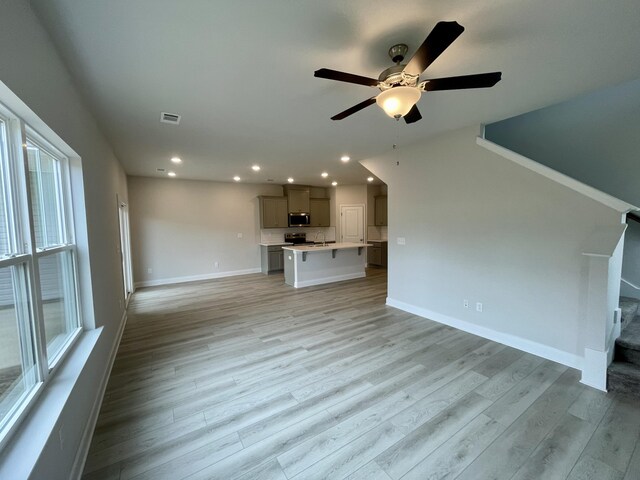 unfurnished living room with light wood-type flooring, ceiling fan, a healthy amount of sunlight, and sink