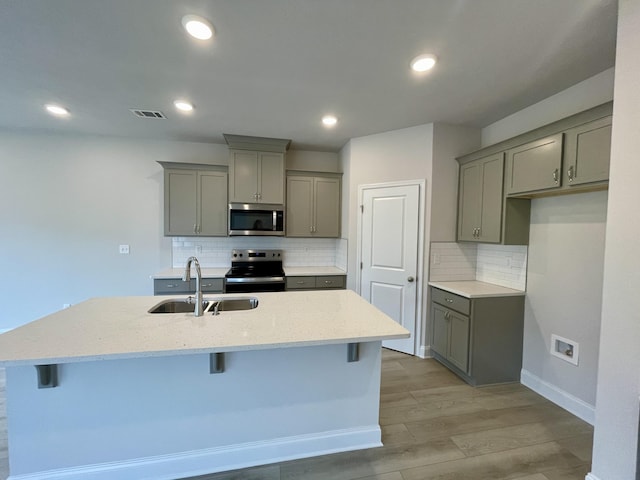 kitchen featuring gray cabinetry, sink, stainless steel appliances, an island with sink, and a breakfast bar