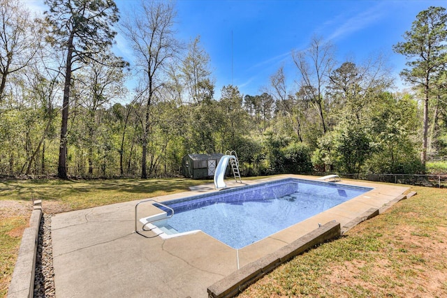outdoor pool featuring a storage shed, a water slide, a lawn, fence, and an outbuilding