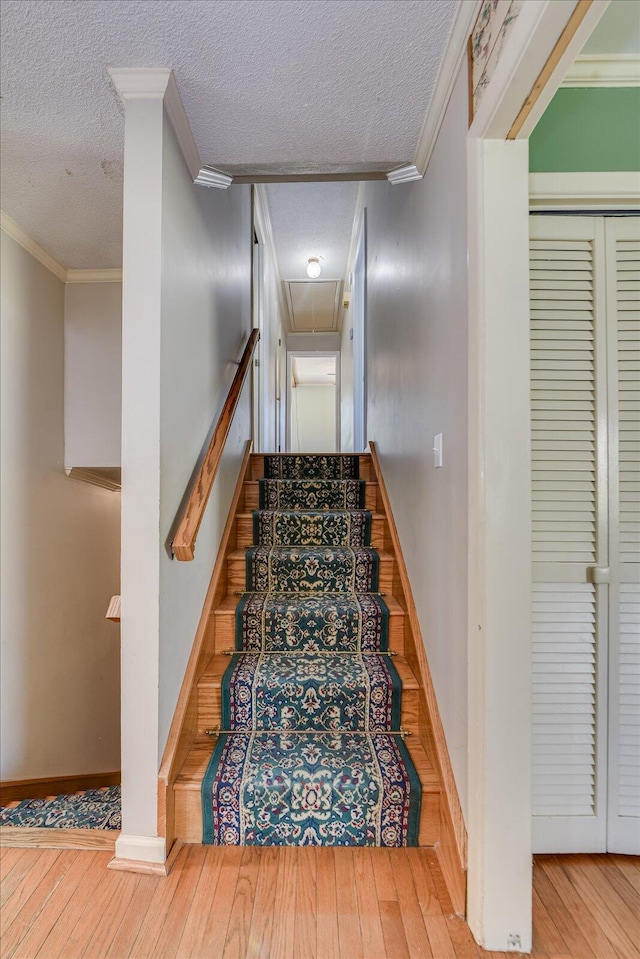 staircase with hardwood / wood-style floors, a textured ceiling, attic access, and crown molding