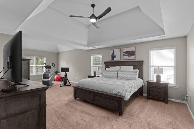 bedroom featuring light colored carpet, a tray ceiling, and baseboards