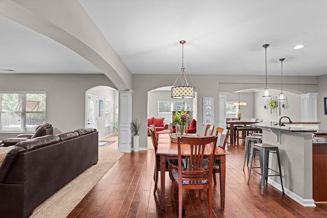 dining room featuring arched walkways, dark wood finished floors, recessed lighting, baseboards, and ornate columns