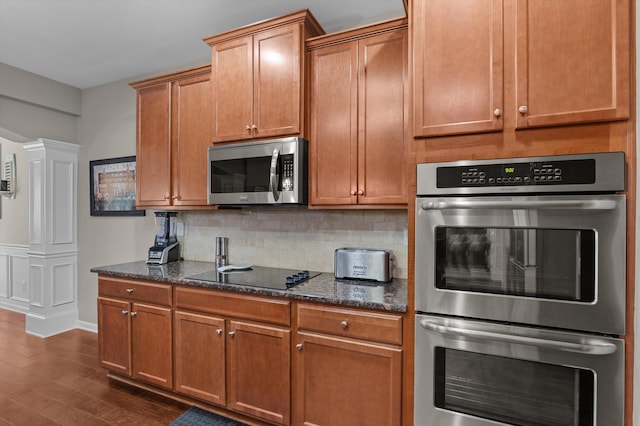 kitchen featuring stainless steel appliances, tasteful backsplash, ornate columns, dark wood-type flooring, and dark stone counters