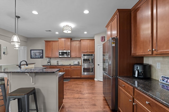 kitchen featuring appliances with stainless steel finishes, brown cabinets, a kitchen breakfast bar, dark wood-style flooring, and tasteful backsplash