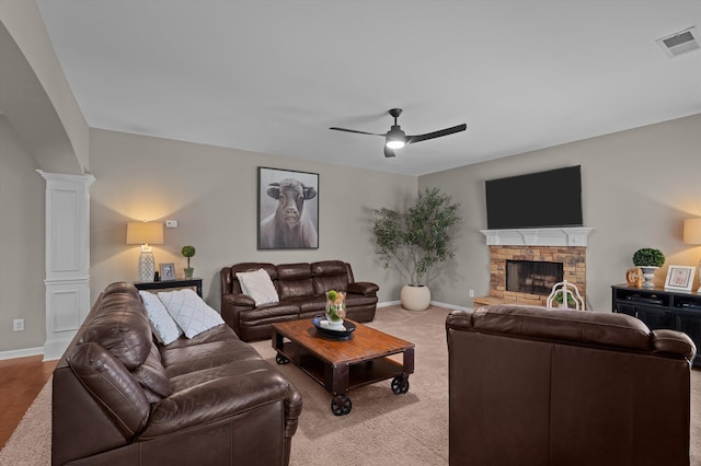 carpeted living area with decorative columns, ceiling fan, a fireplace, and baseboards