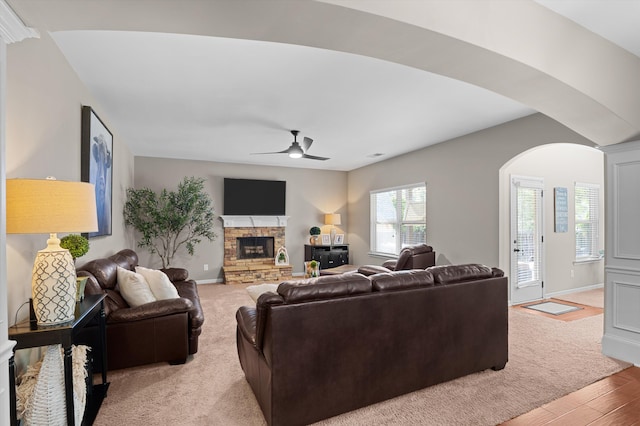 living room with a ceiling fan, a fireplace, arched walkways, and baseboards